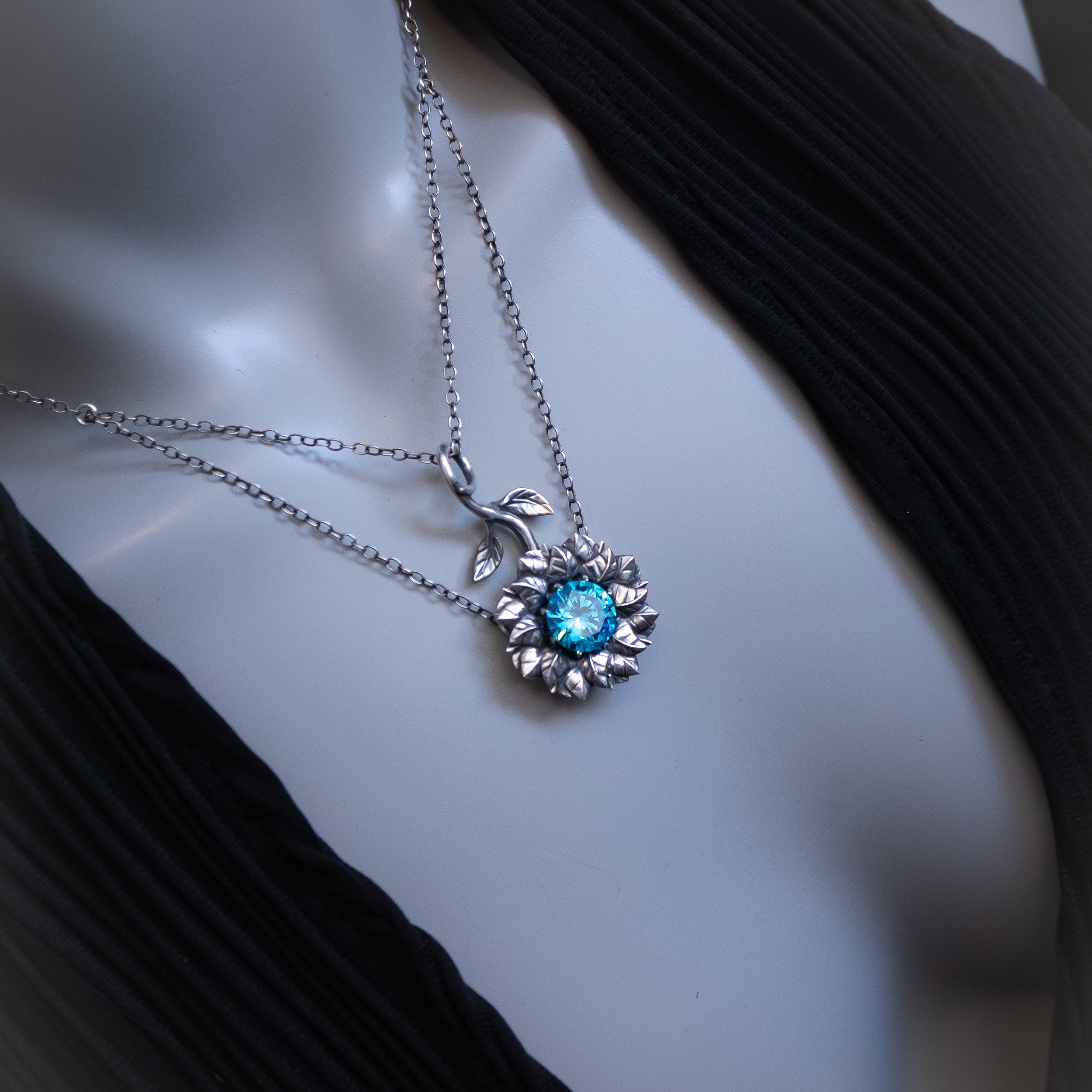 Silver necklace with a blue gemstone pendant on a mannequin bust.