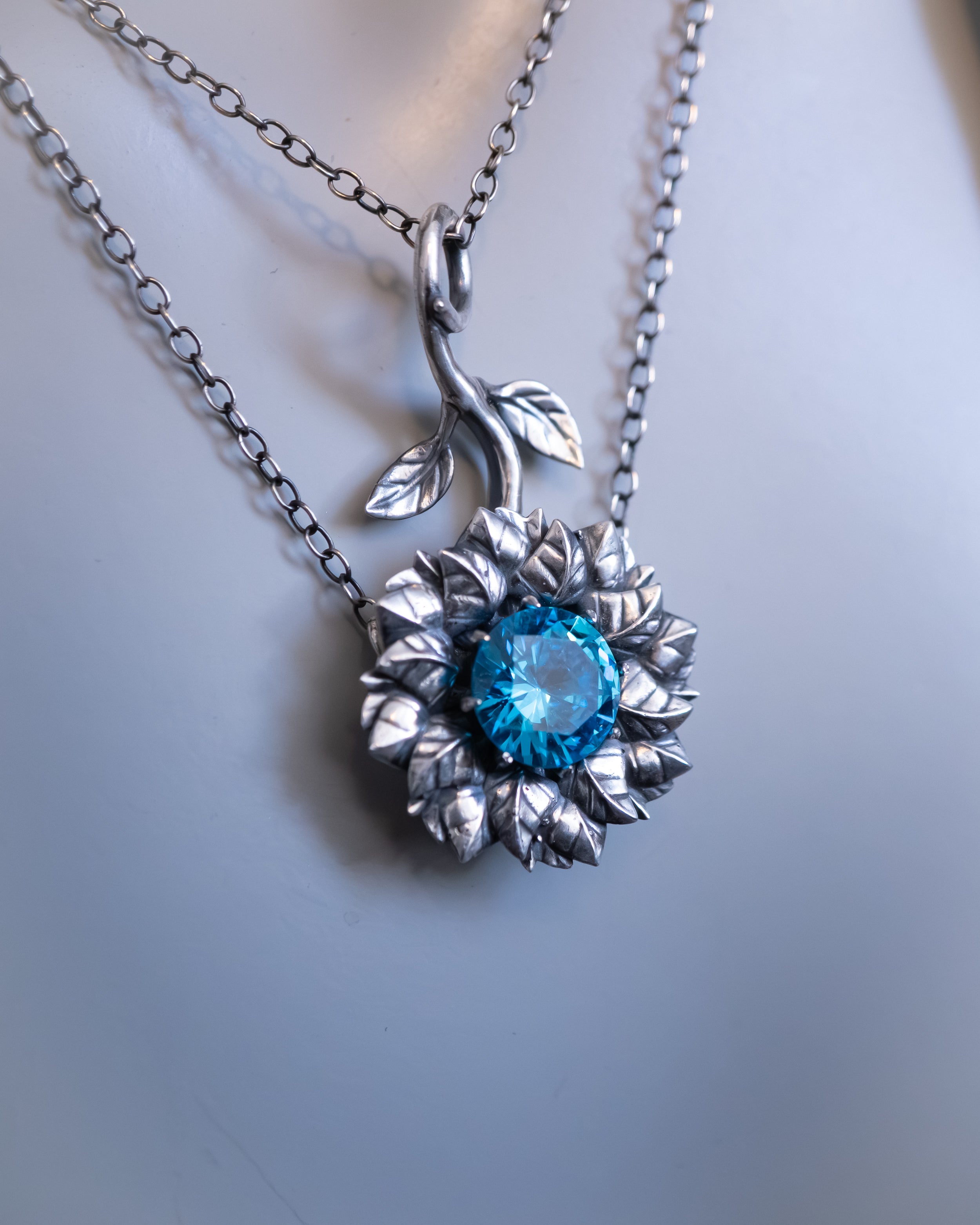 Silver pendant with a blue gemstone on a light gray background