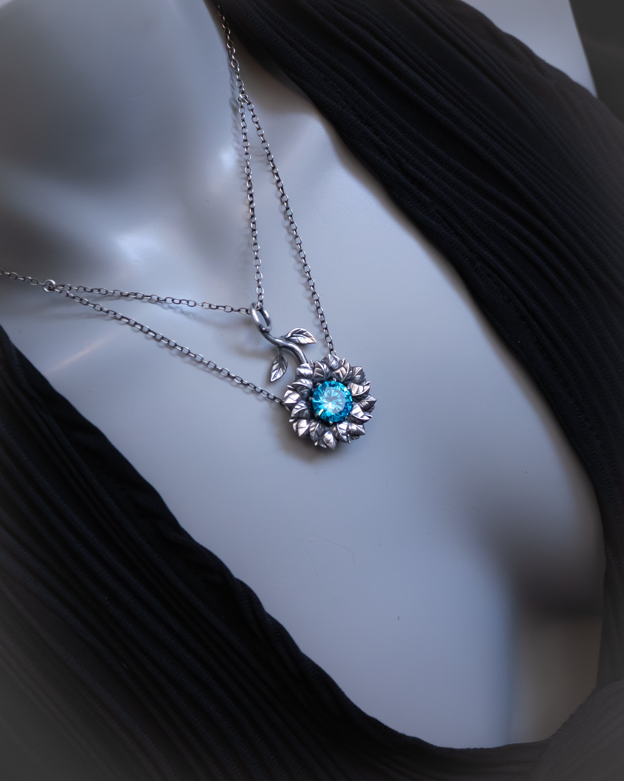 Silver necklace with a blue gemstone pendant on a mannequin bust.
