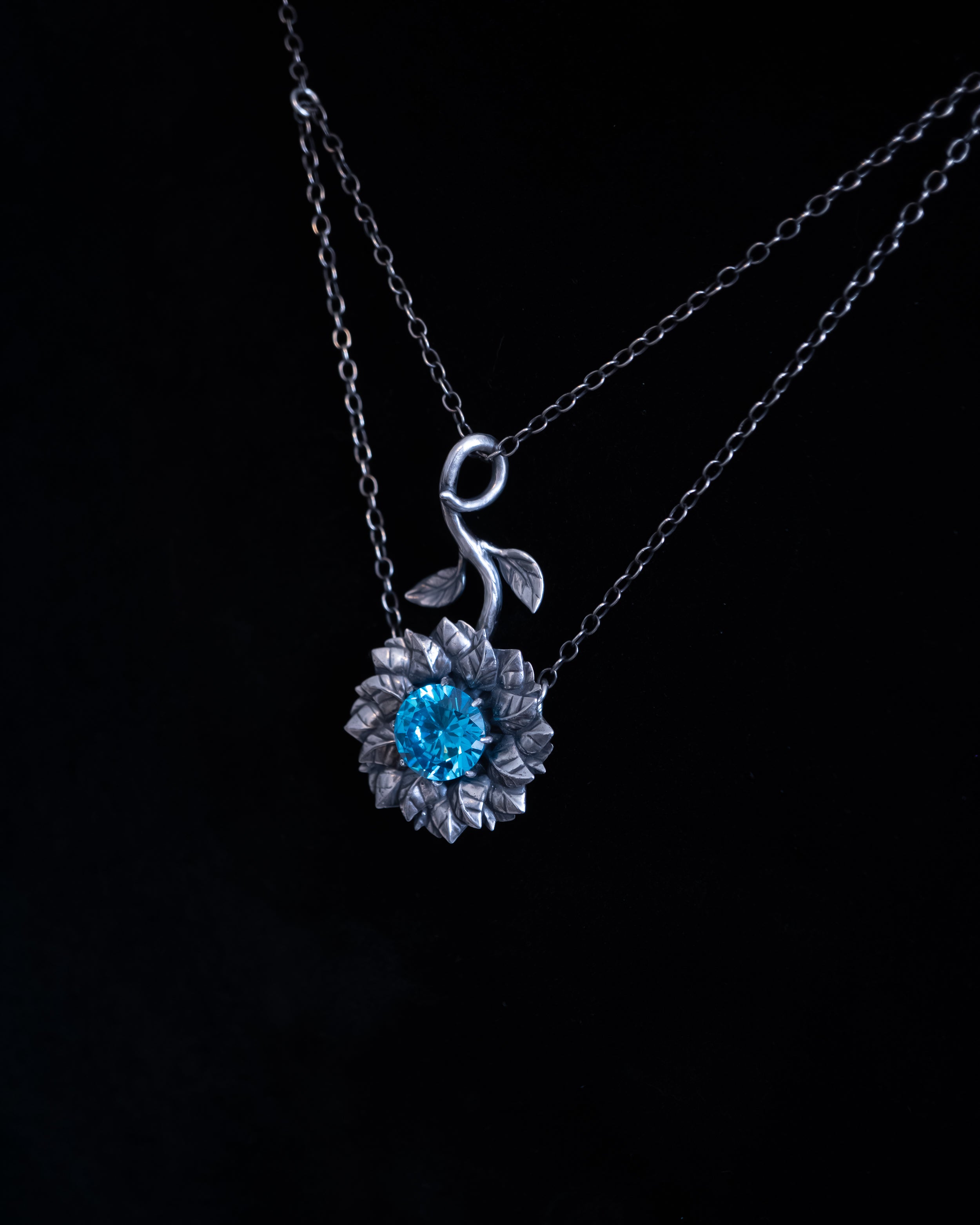Silver necklace with a blue gemstone pendant on a black background
