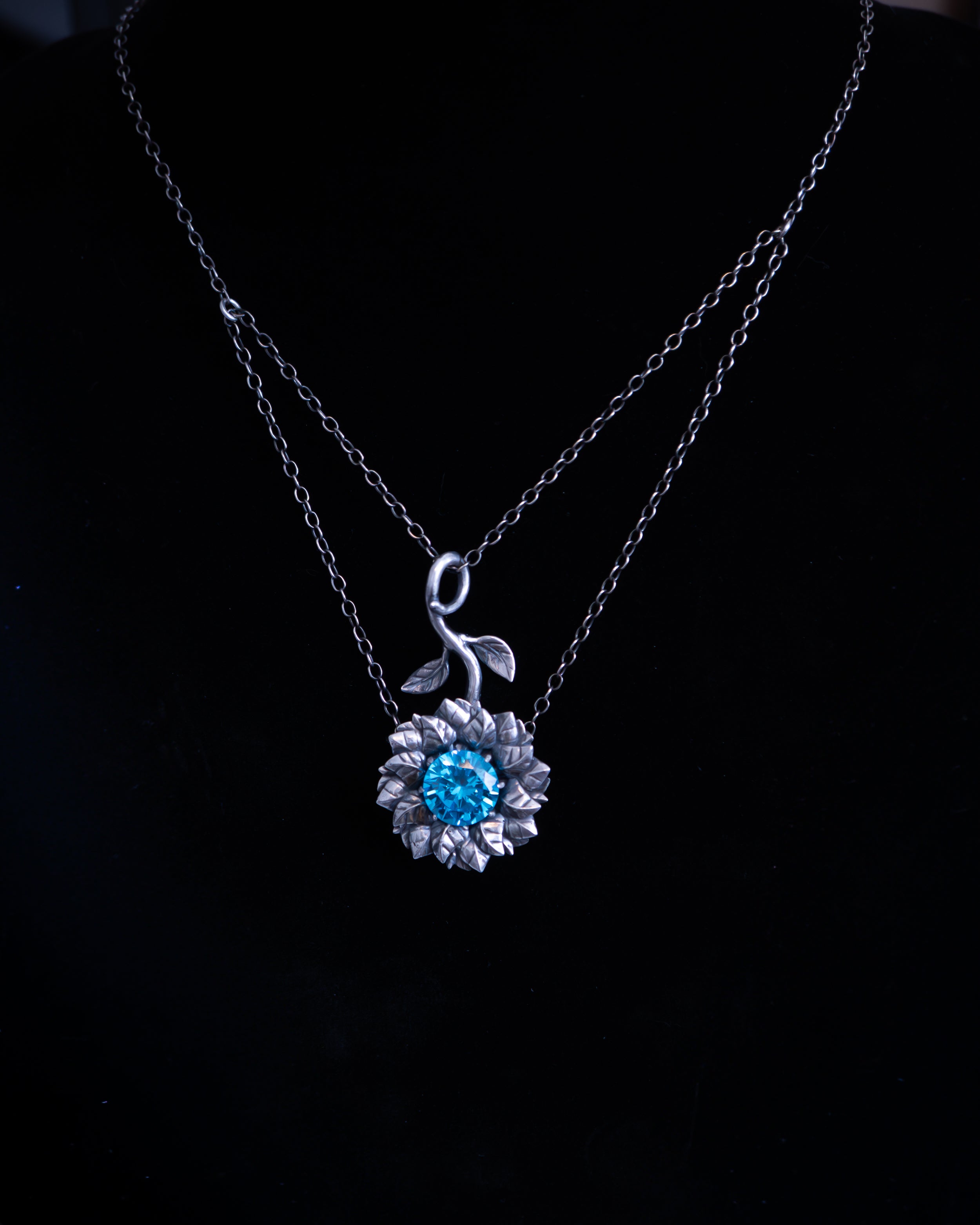 Silver necklace with a blue gemstone pendant on a black background