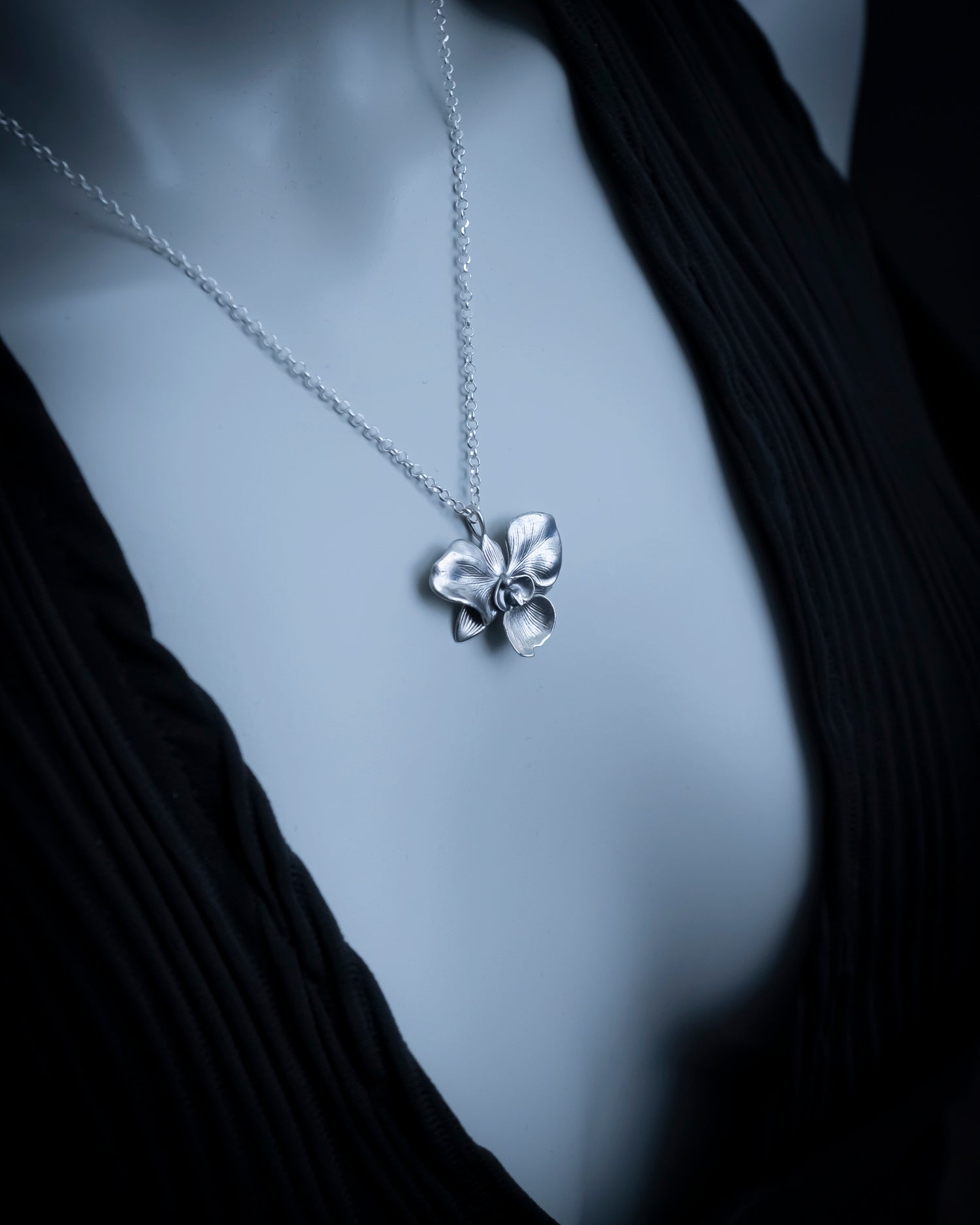 Silver flower pendant necklace on a black garment against a gray background