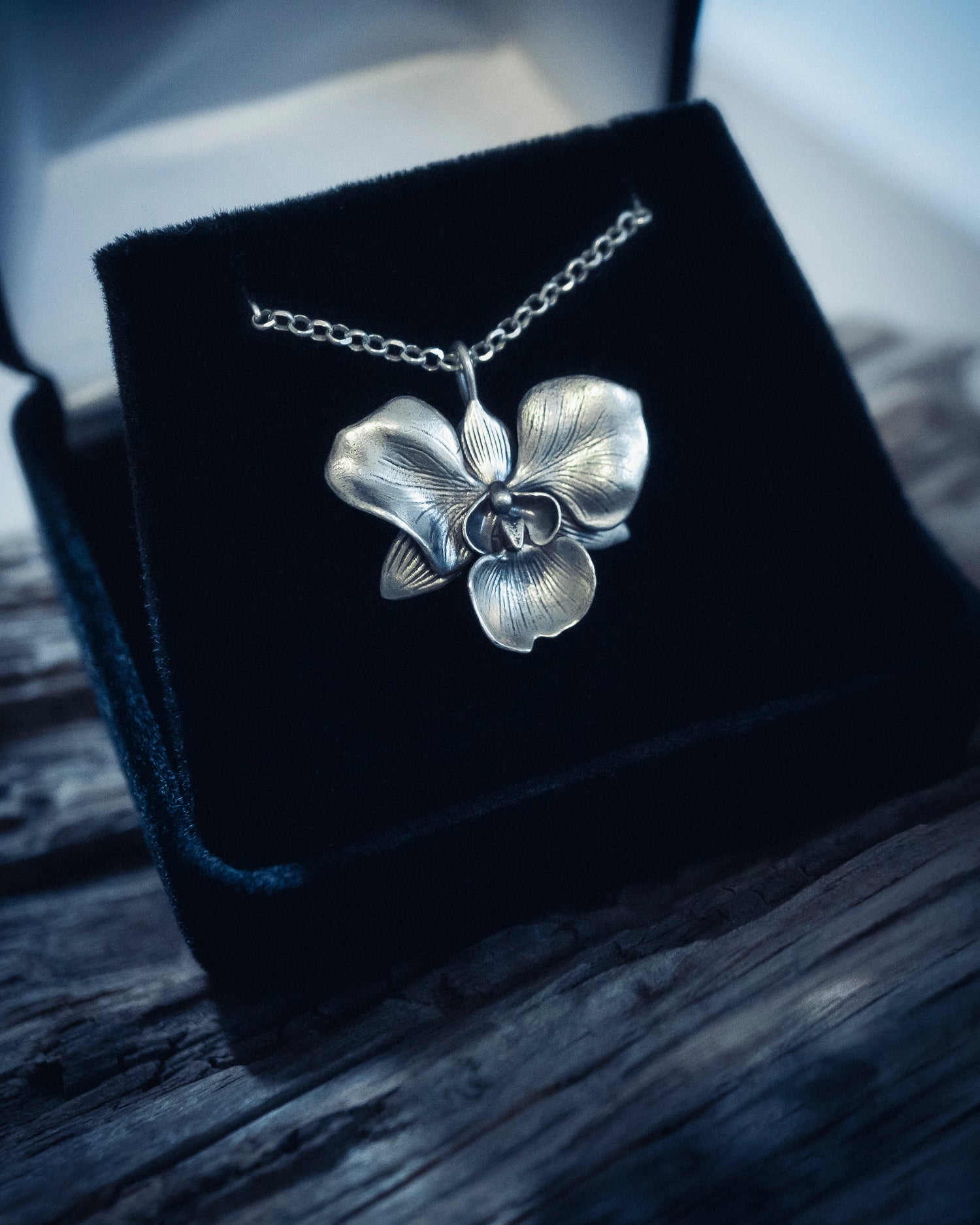 Silver orchid necklace on a black velvet cushion