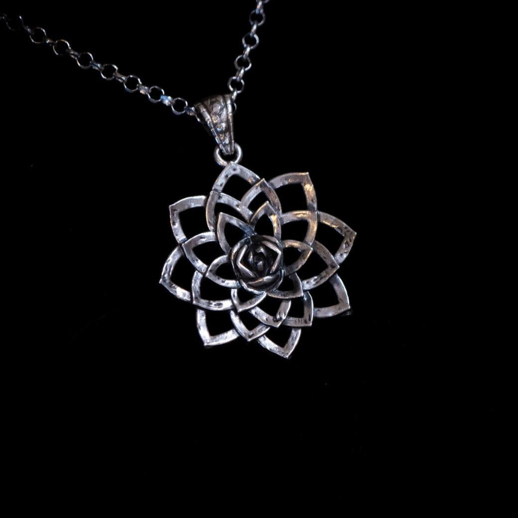 Silver flower-shaped pendant on a chain against a black background