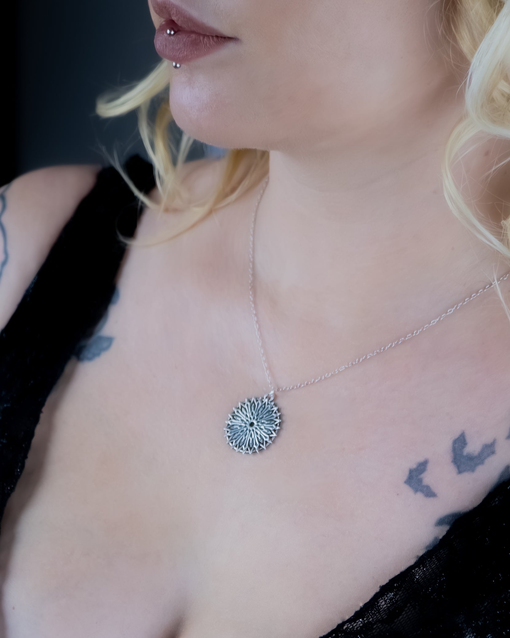 Close-up of a necklace with a circular pendant worn by a person with tattoos.
