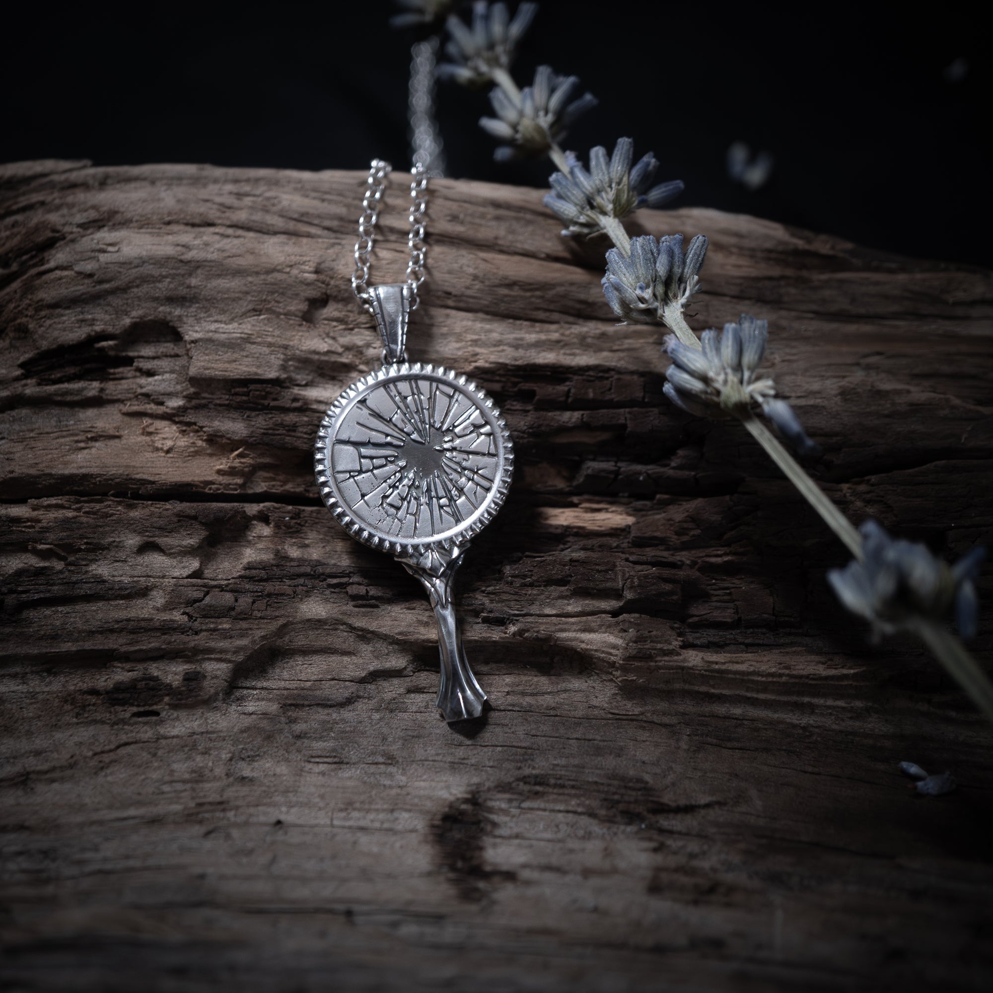 Silver broken mirror necklace with pendant on a wooden surface with dried lavender.