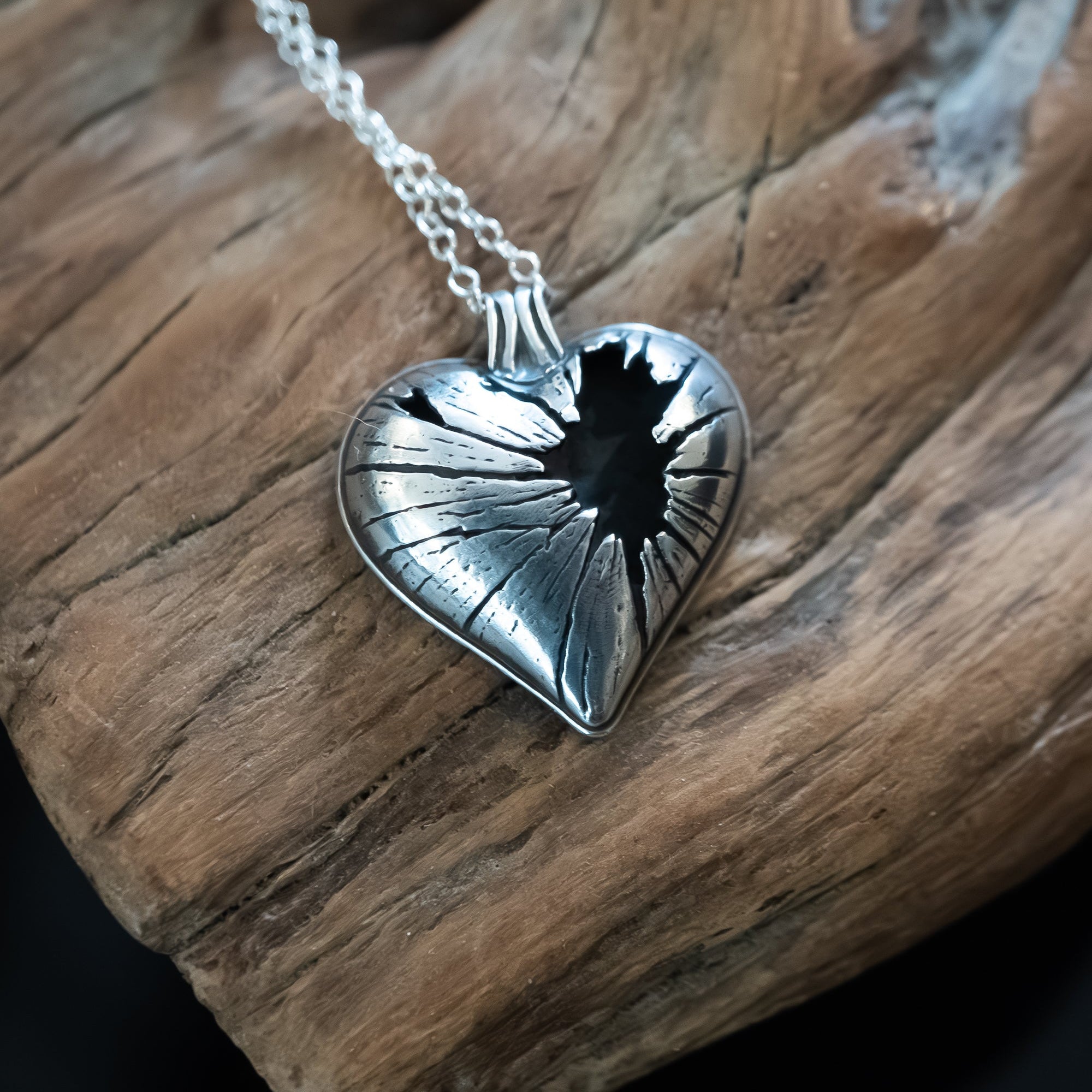 Silver heart-shaped pendant on a chain against a driftwood background