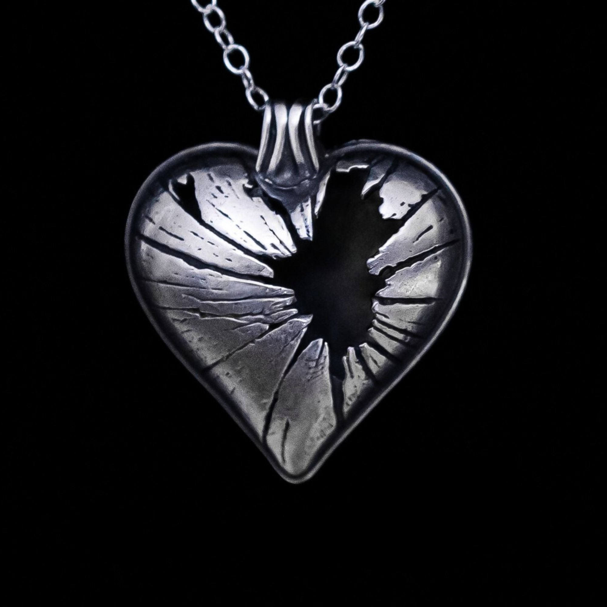 Silver heart-shaped pendant with a shattered glass design on a black background, featuring the brand &