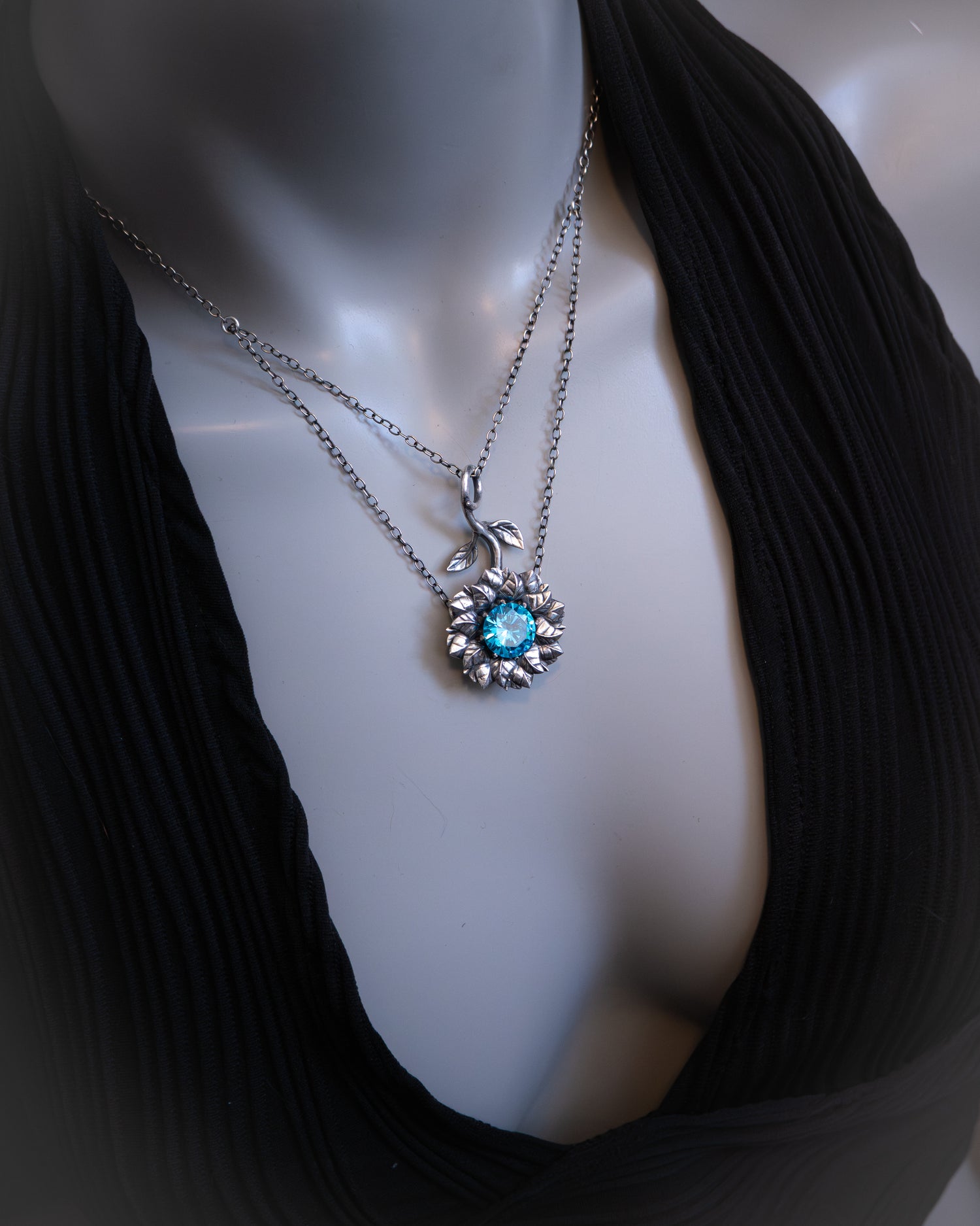 Mannequin wearing a black top with a silver necklace featuring a blue gemstone.