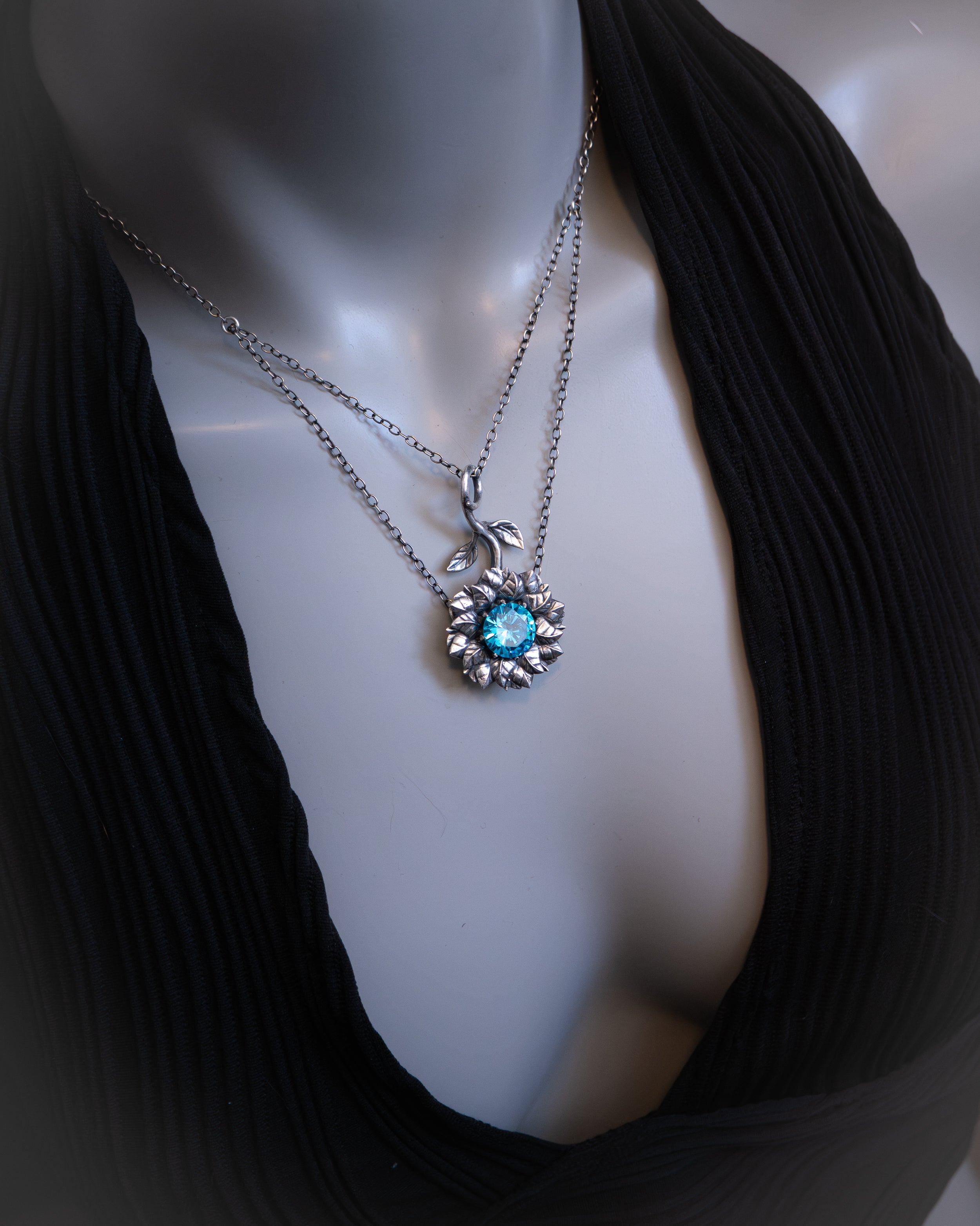 Mannequin wearing a black top with a silver necklace featuring a blue gemstone.