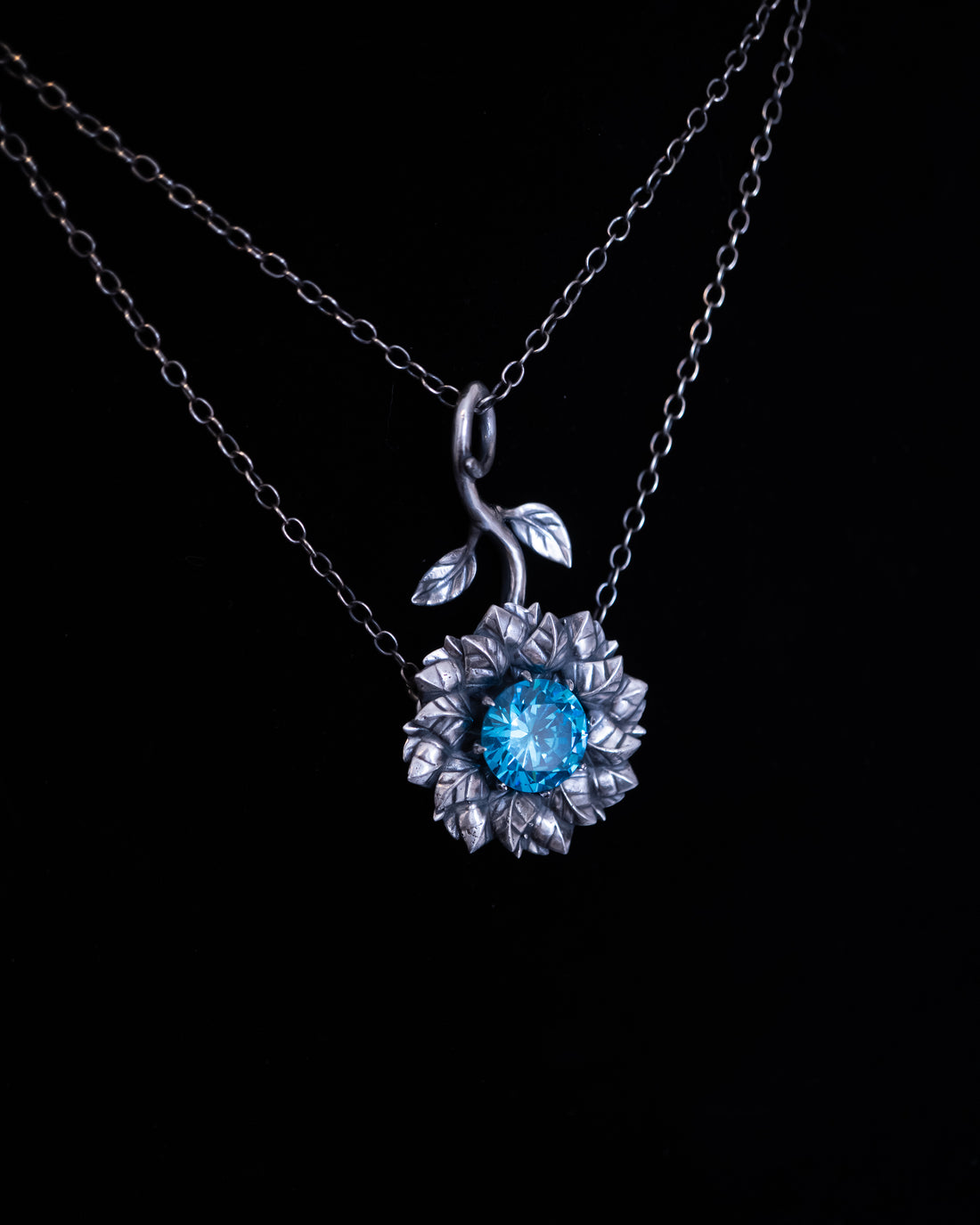 Silver necklace with a flower pendant featuring a blue gemstone on a black background