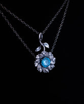 Silver necklace with a flower pendant featuring a blue gemstone on a black background