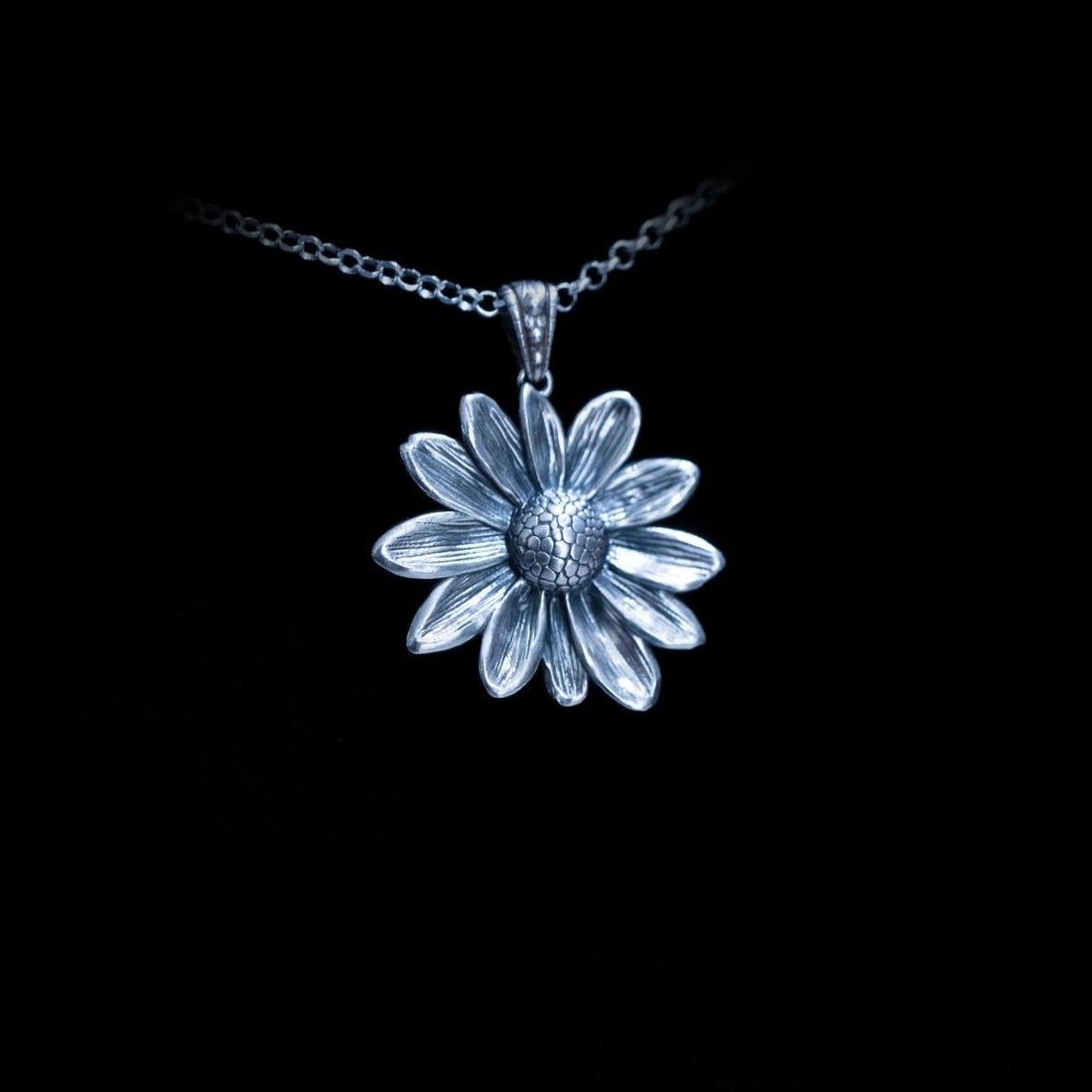 Silver daisy pendant on a black background.