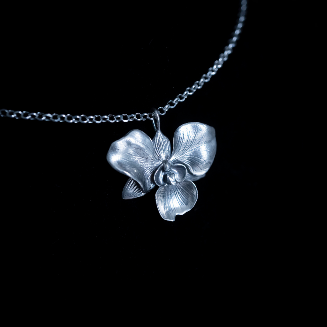 A sterling silver floral pendant, specifically an orchid, against a black background 
