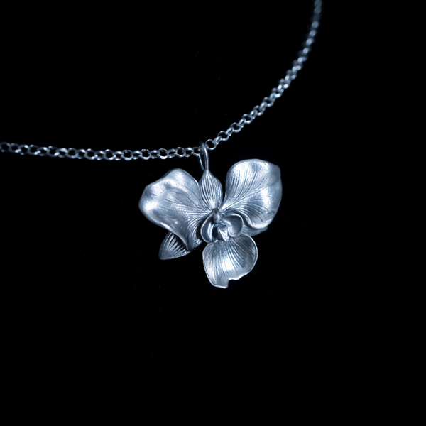 A sterling silver floral pendant, specifically an orchid, against a black background 