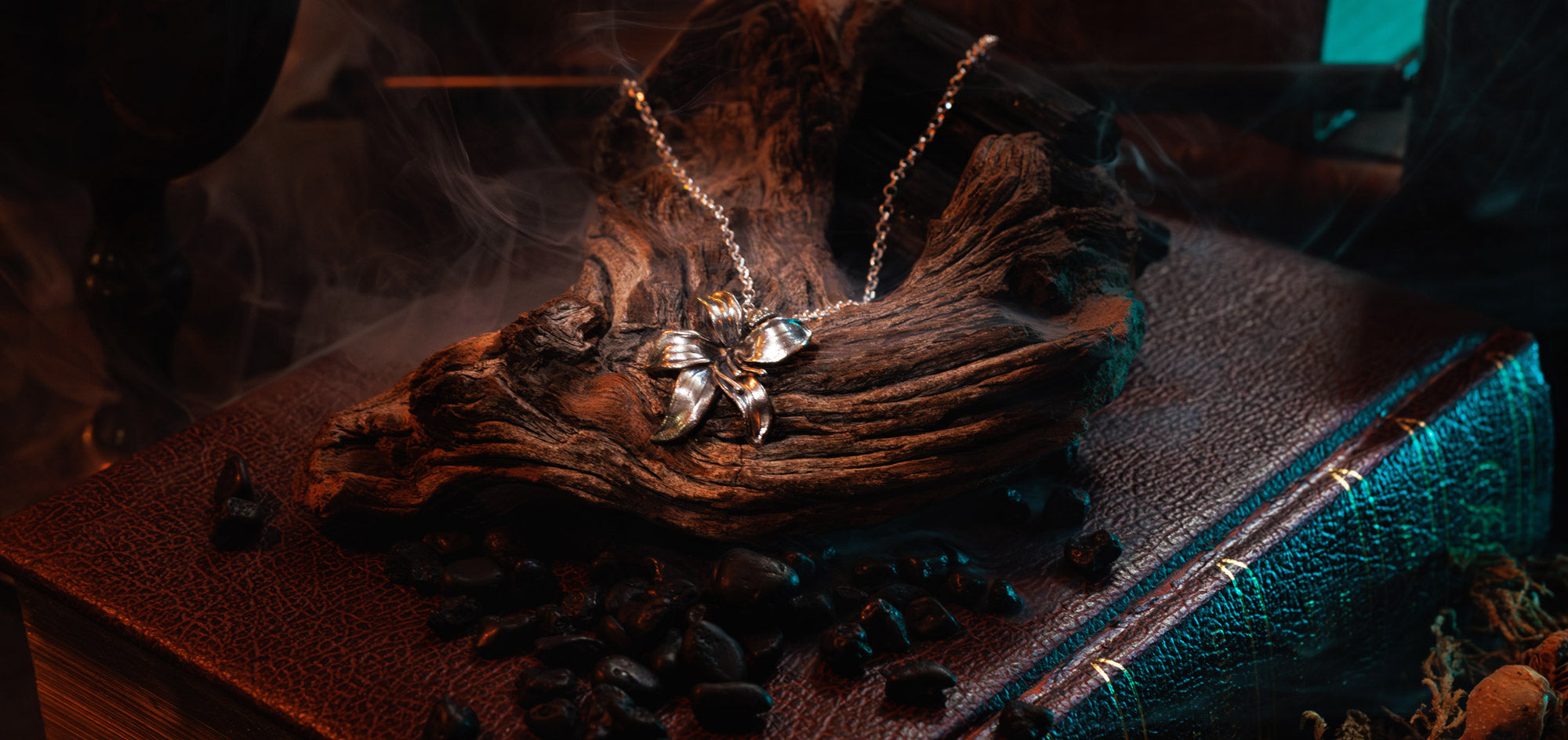 silver lilly necklace on a book with smoke rising, on a dark background.