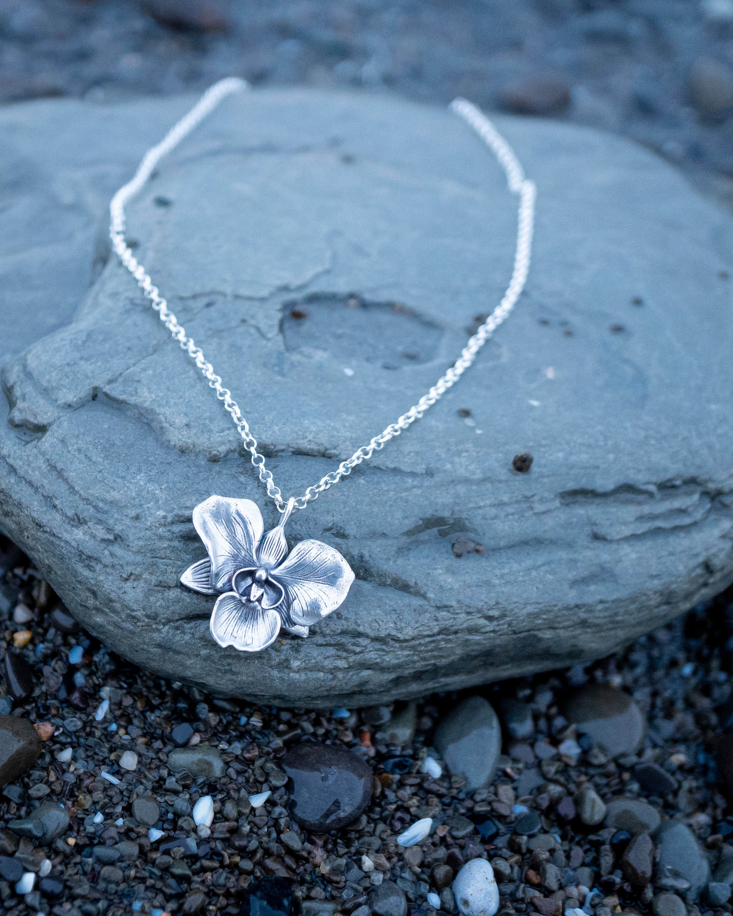 Silver flower pendant necklace on a rock with a natural background
