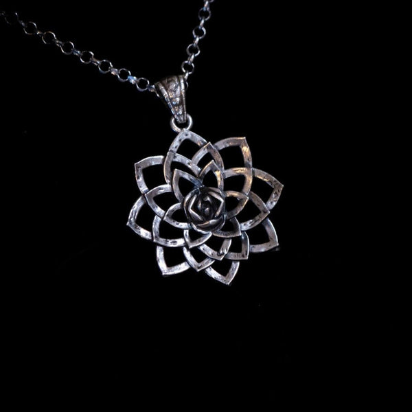 Silver flower-shaped pendant on a chain against a black background