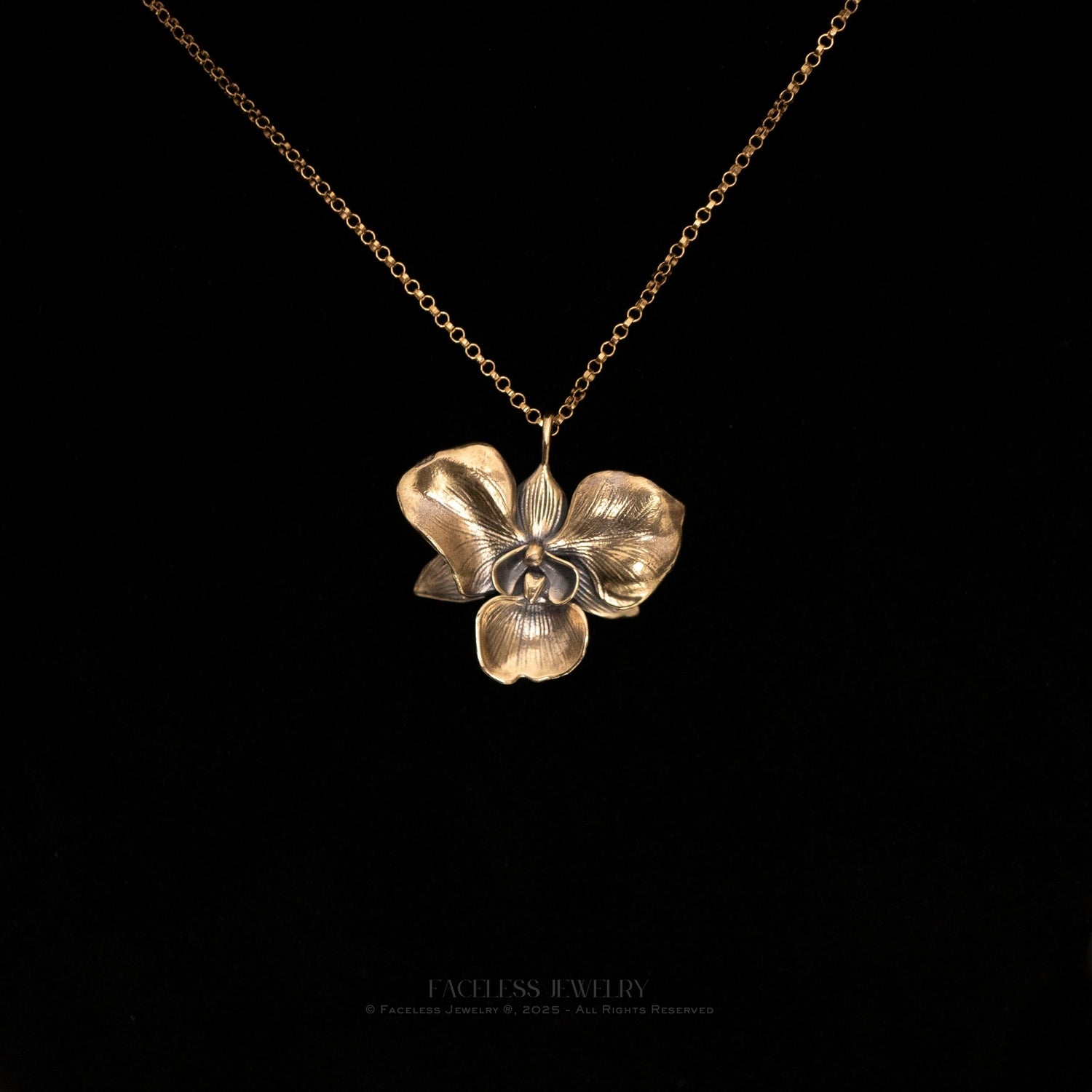 The Golden Orchid pendant by Faceless Jewelry displayed against a black background, featuring a 14Kt gold orchid flower with finely detailed petals and a warm, polished finish, hanging from a delicate gold rolo chain.