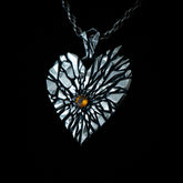 A heart-shaped pendant necklace with a textured, cracked metallic finish and a small amber gemstone at the center, suspended on a dark chain against a solid black background.