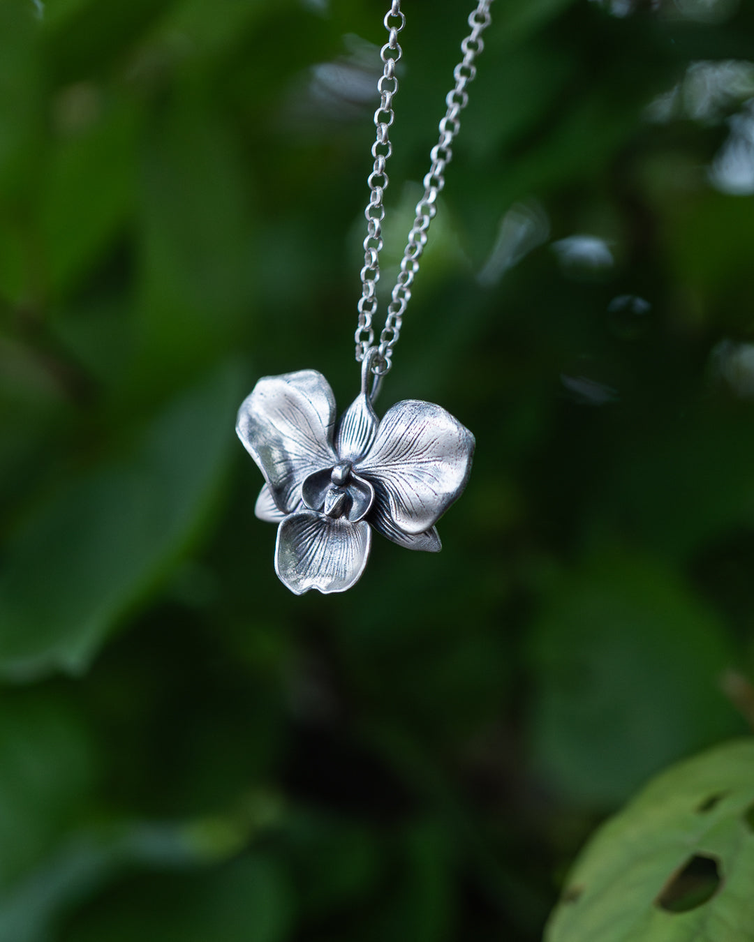 Silver orchid flower necklace against a green leafy background