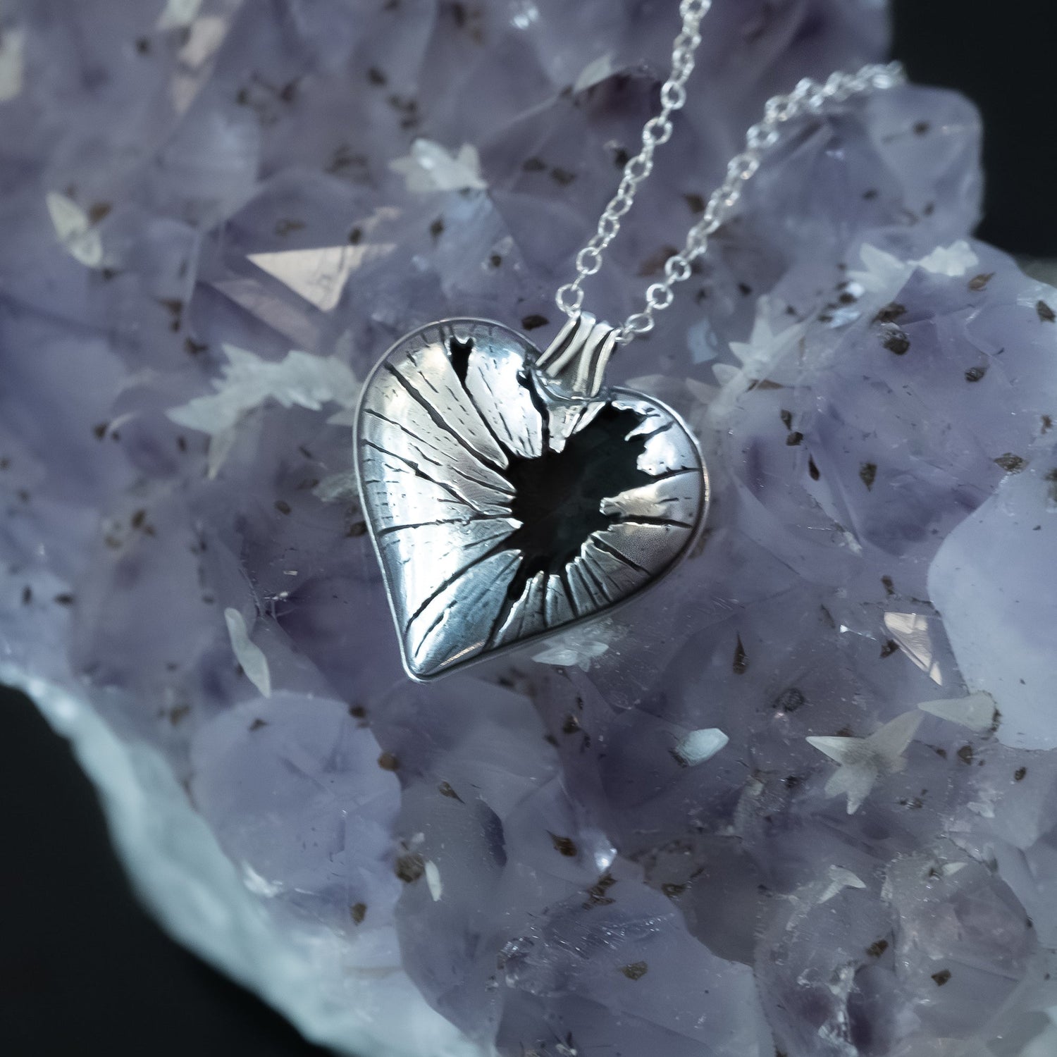 Broken heart necklace in sterling silver resting on a bed of raw purple amethyst chrystal with inclusions